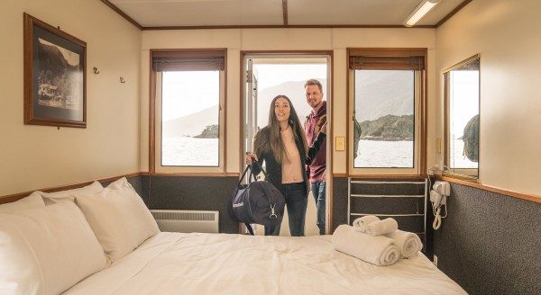 Two people standing in a doorway with a bed infront of them on a boat at Doubtful Sound