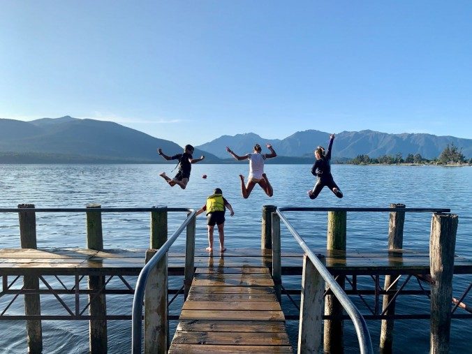 children jumping off wharf into lake with mountains in the background