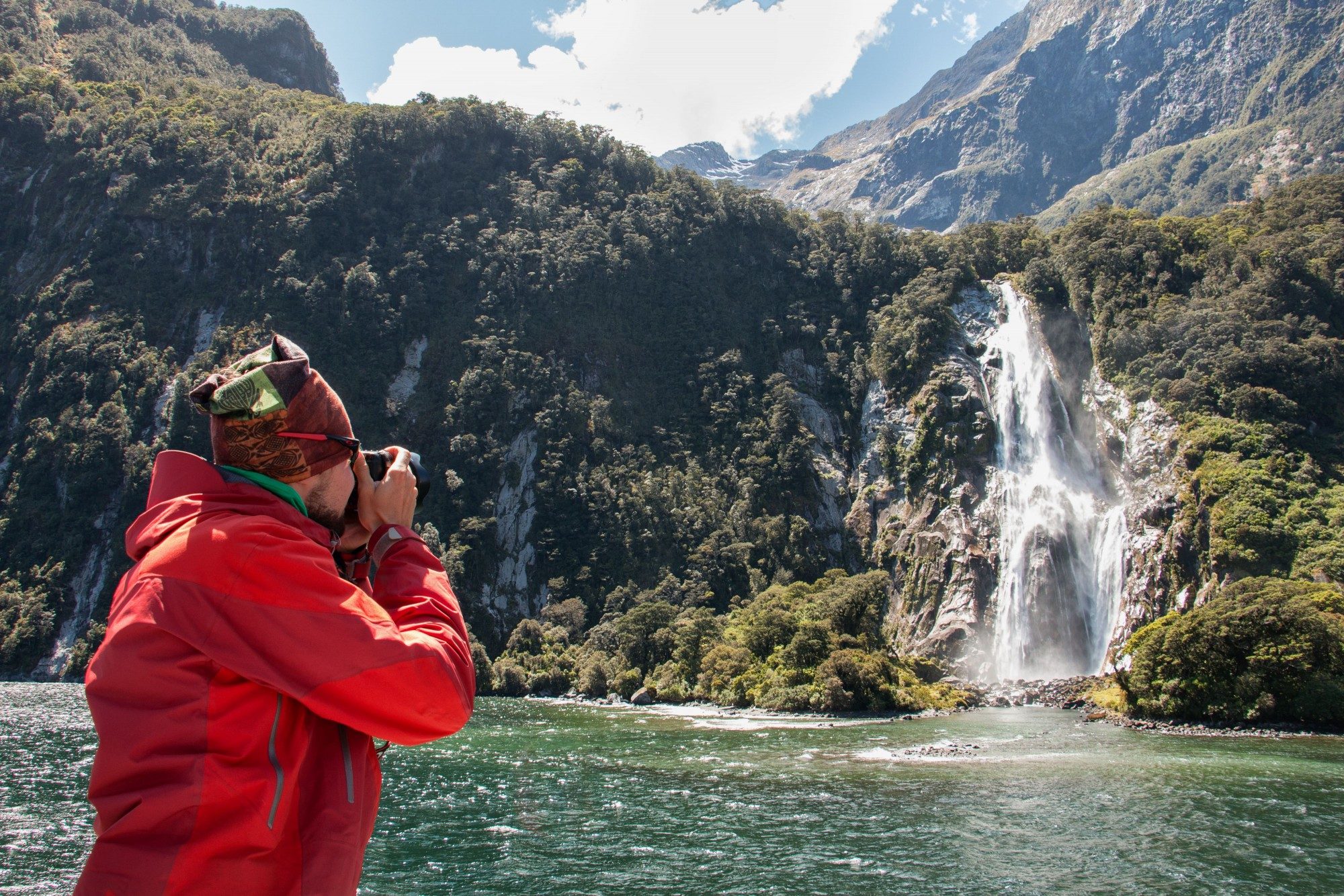 Lady Bowen Falls waterfall at Milford Sound being photographed by a man in a red coat